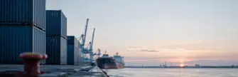 נמל מסחרי באירופה עם מכולות ואונייה בשעת זריחה
